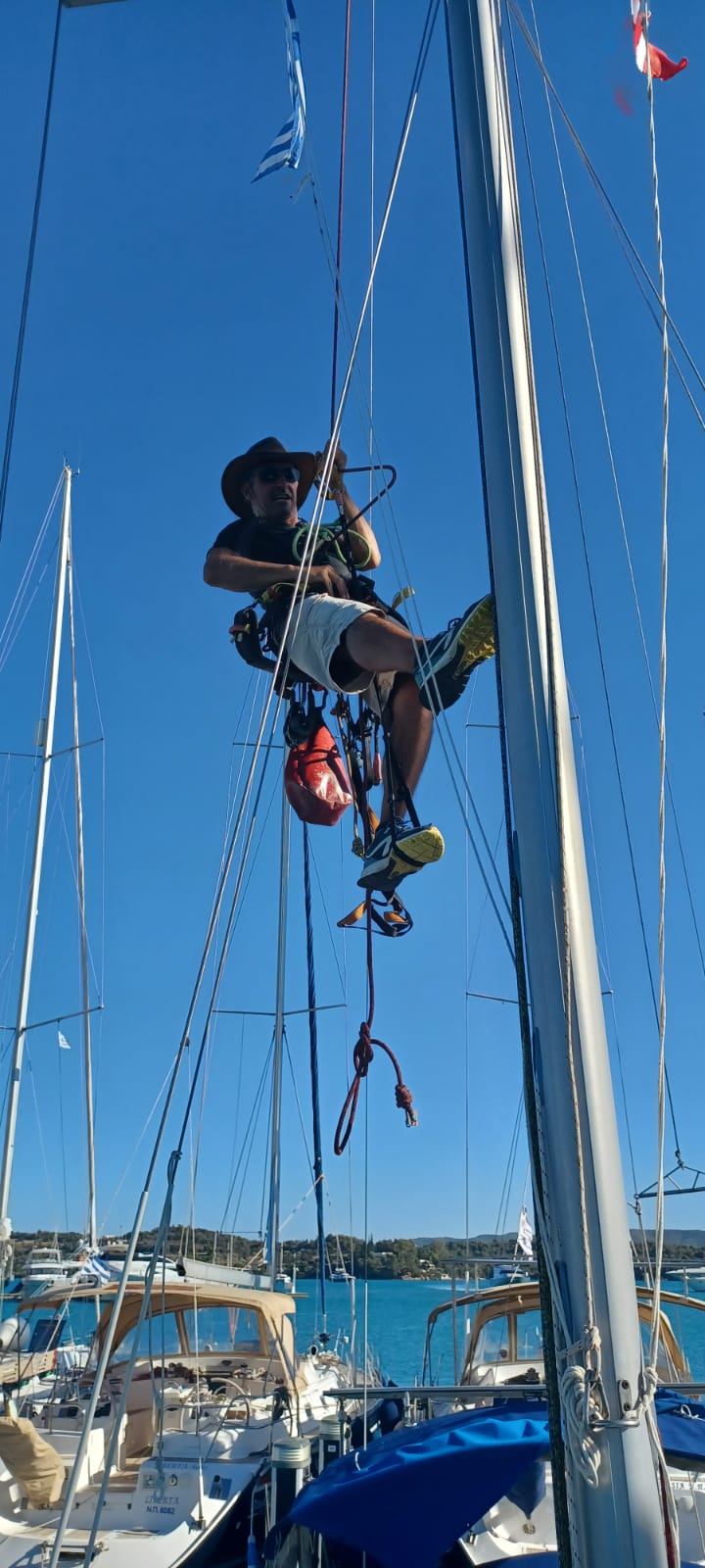 Un homme grimpe au mât d'un voilier sous un ciel bleu.