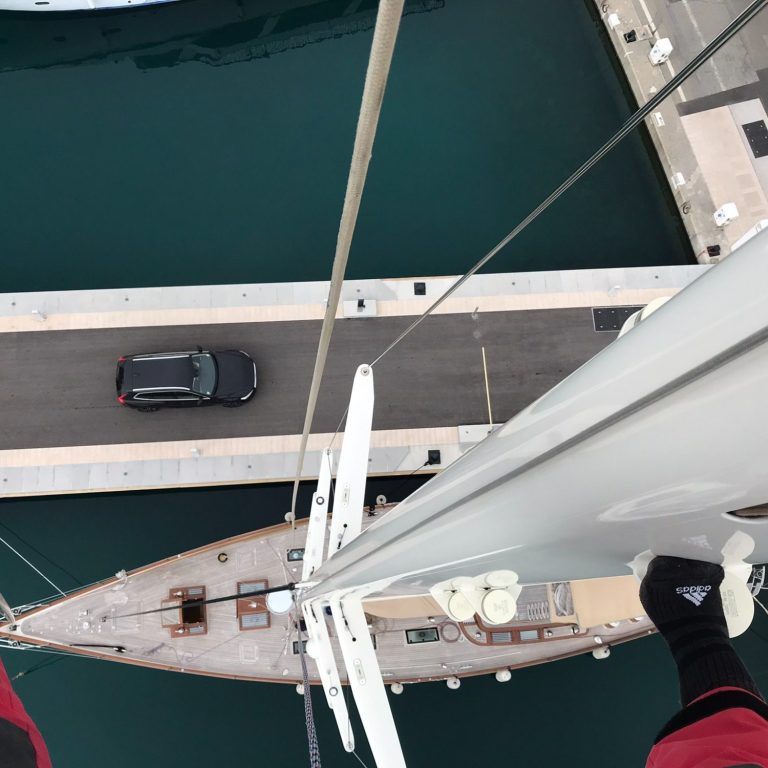 Travail en hauteur sur un mat de voilier Vue du haut d'un mât de bateau, sur un quai.